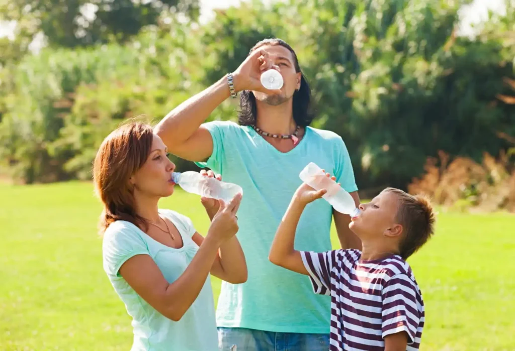 Adults and children drinking water throughout the day with hydration guidelines and healthy lifestyle elements in the background.