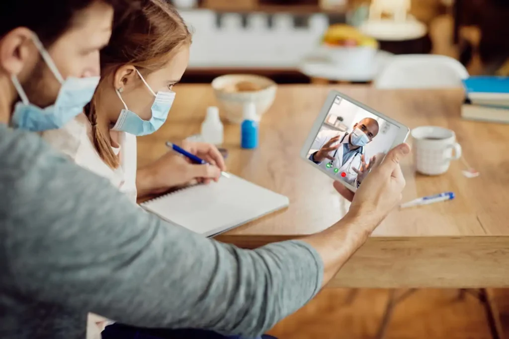 Patient attending a telehealth appointment on a laptop with medical notes, identification, and prescribed medications ready for an online doctor consultation.